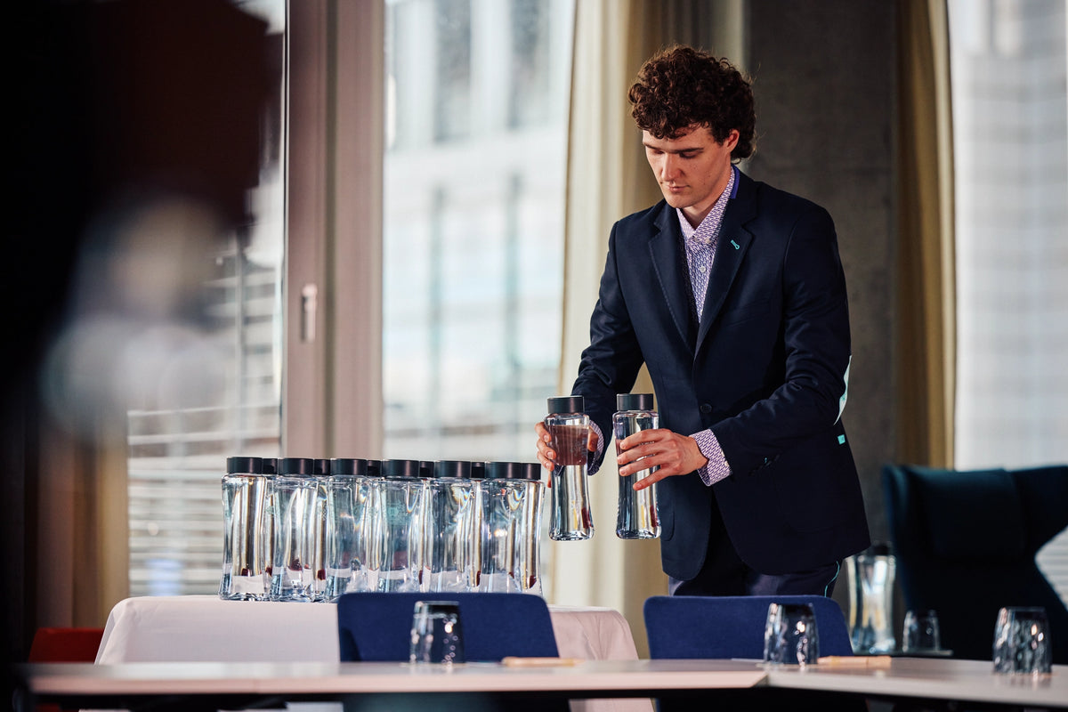 Waiter in a suit holding water bottles, while preparing a meeting room table.